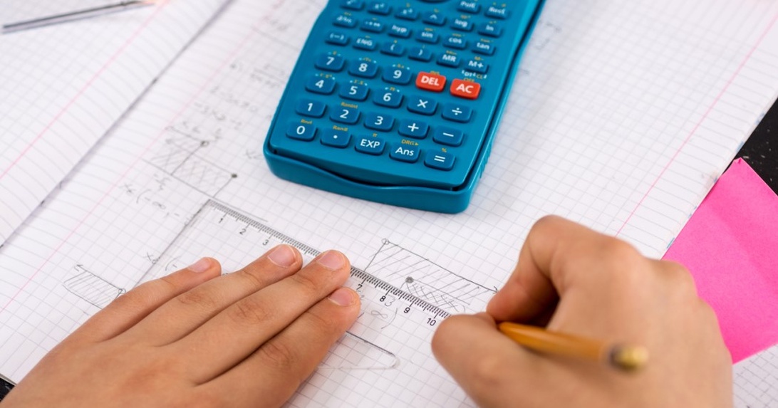 Hände arbeiten an mathematischen Berechnungen auf Millimeterpapier mit Lineal und Taschenrechner.